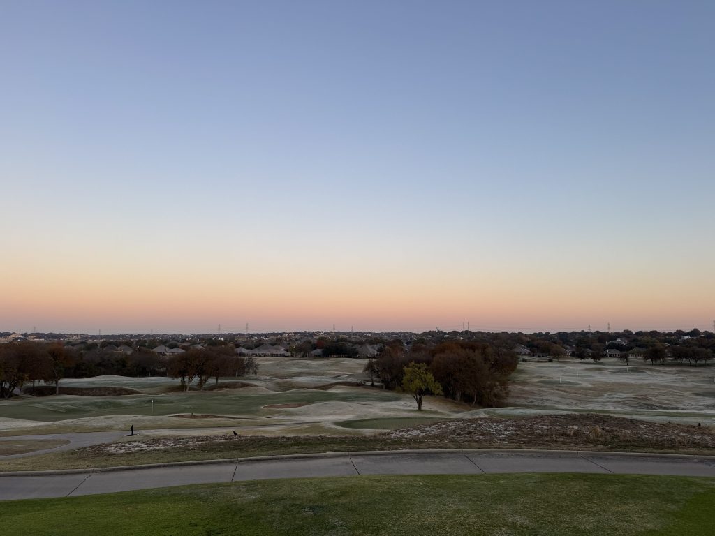 View from a cart path overlooking the course. Trees and dunes dot the landscape on an early morning.